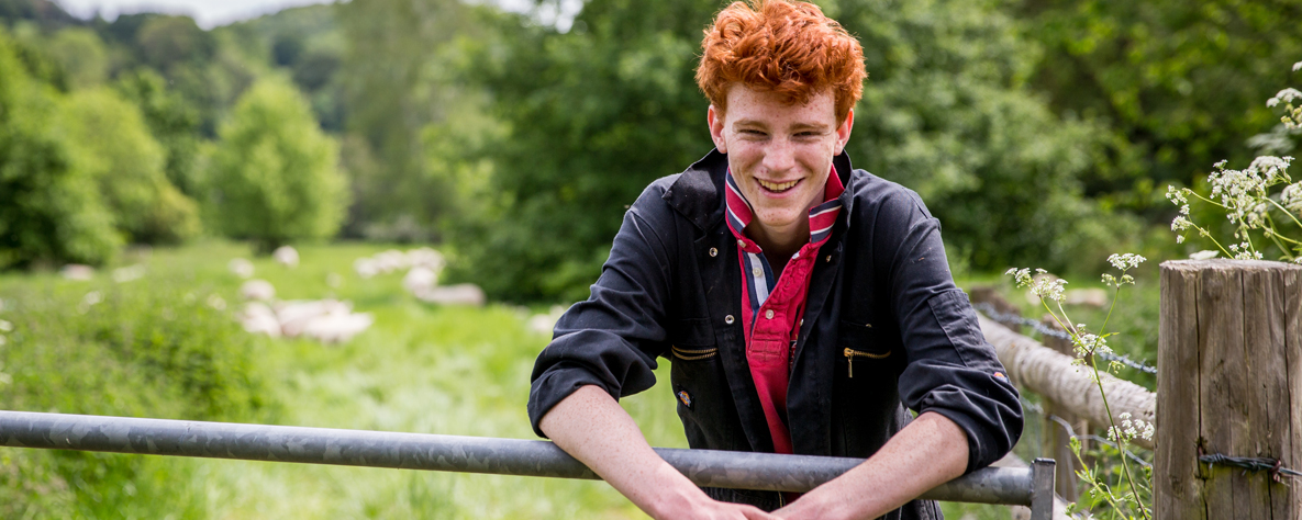 Young farmer leaning on a gate with fields in background