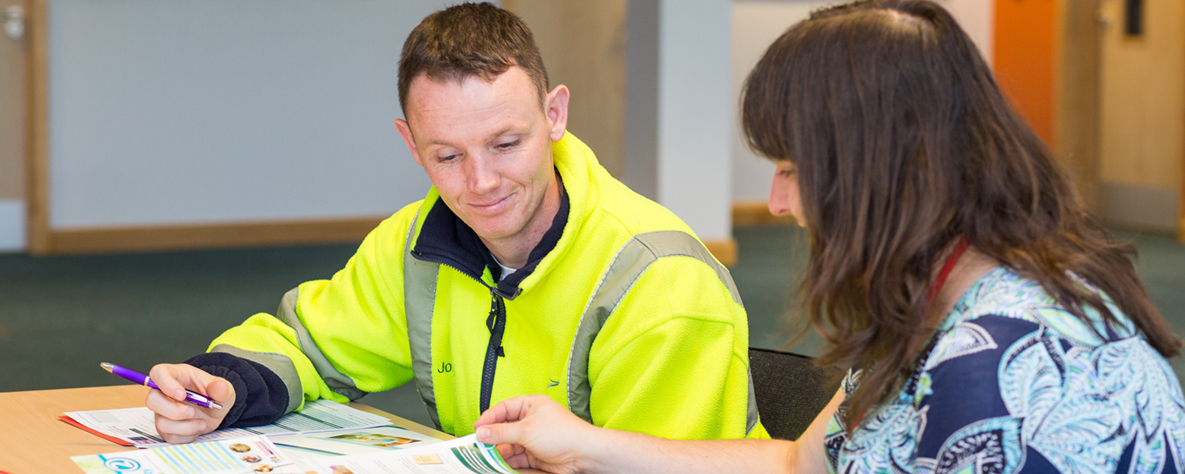 Upskilling at Work staff member sat at desk helping male in hi vis jacket on