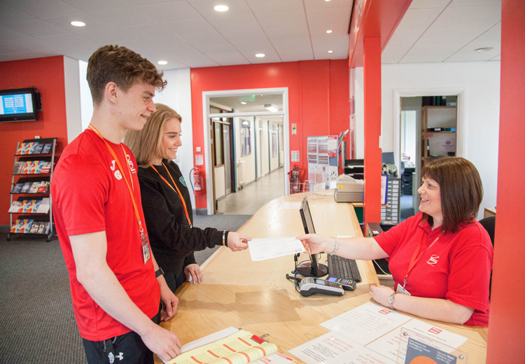 2 students at reception being handed paperwork