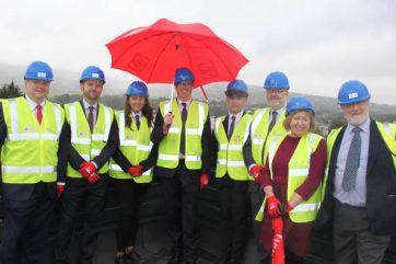 TLZ-topping-out-TBC People in hi viz on the TLZ roof with a red umbrella