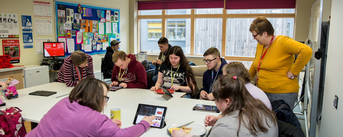 adult skills Group of students sat around a table enjoying a snack and using tablets