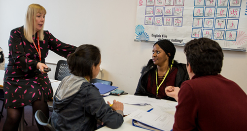 INTL_Courses2 tutor stood talking to a group of learners sat around a table