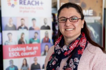 reach-canan Woman standing in front of Reach+ banner