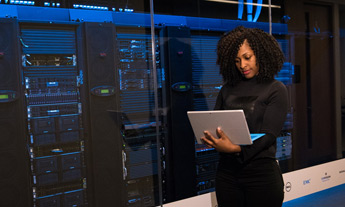 Woman using laptop in front of server racking