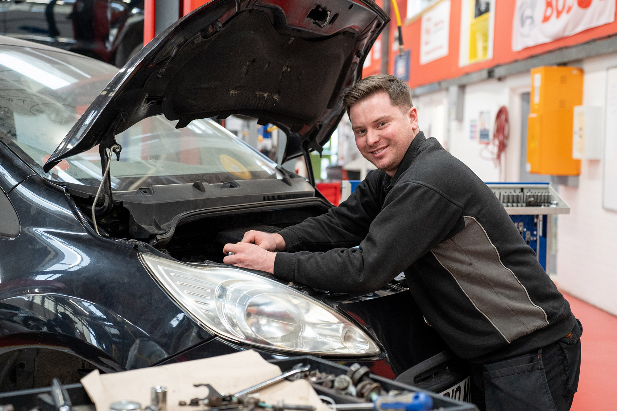 Person leaning over car engine and smiling at the camera