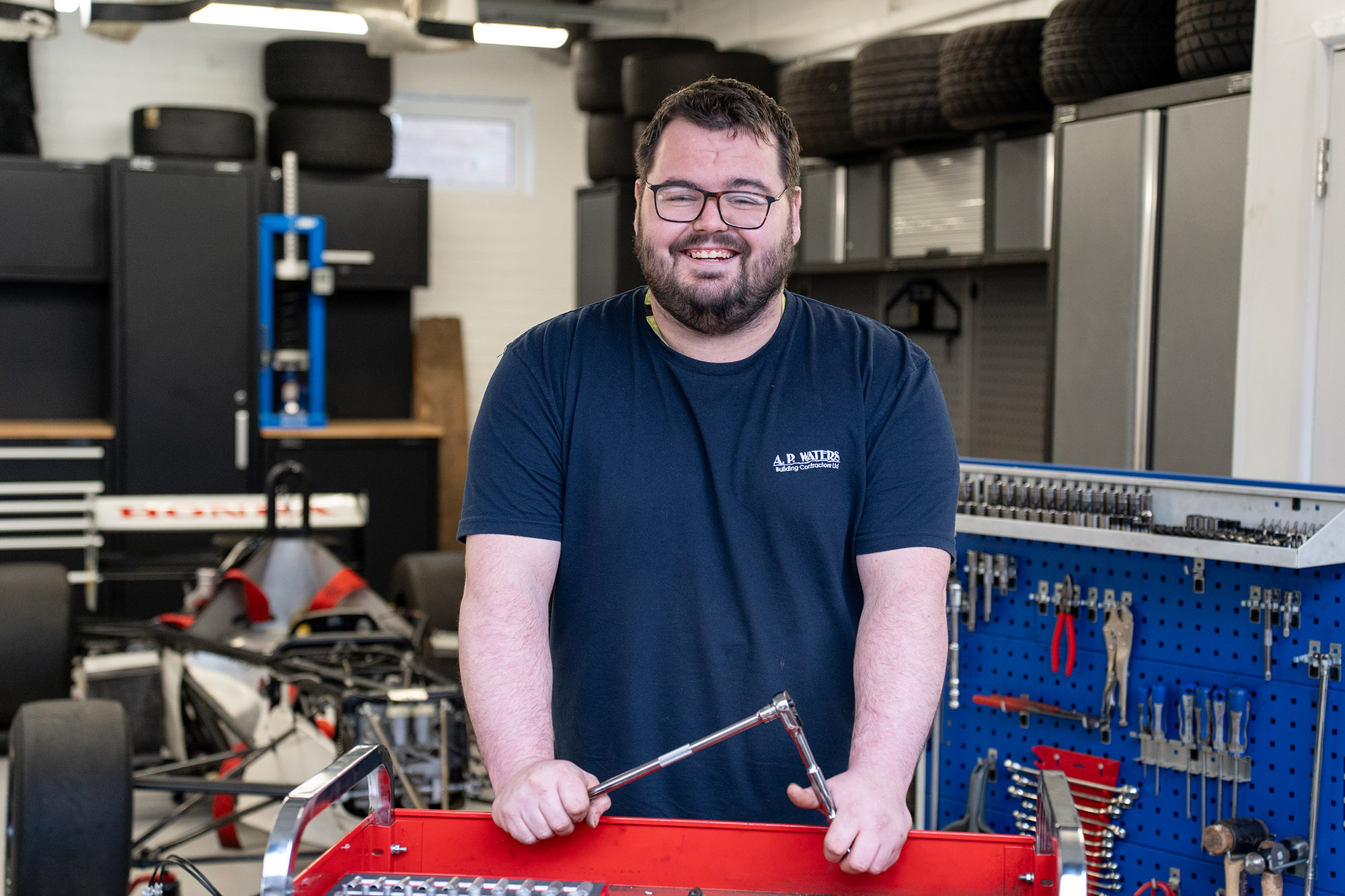 Student holding a wrench over a toolbox, smiling at camera