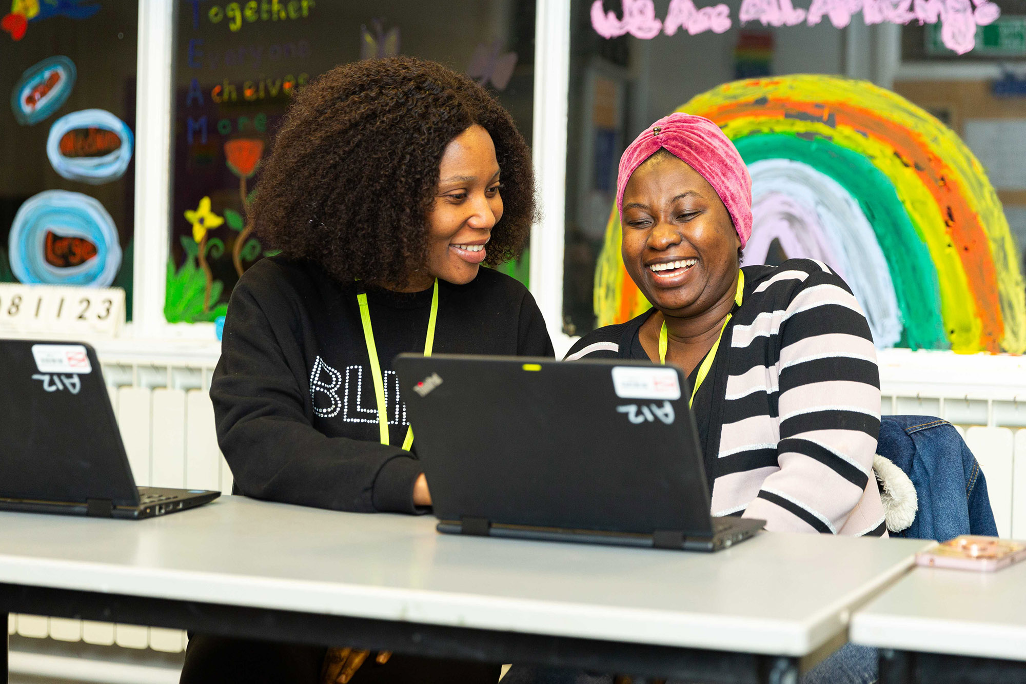 Students smiling in a classroom while working on a laptop