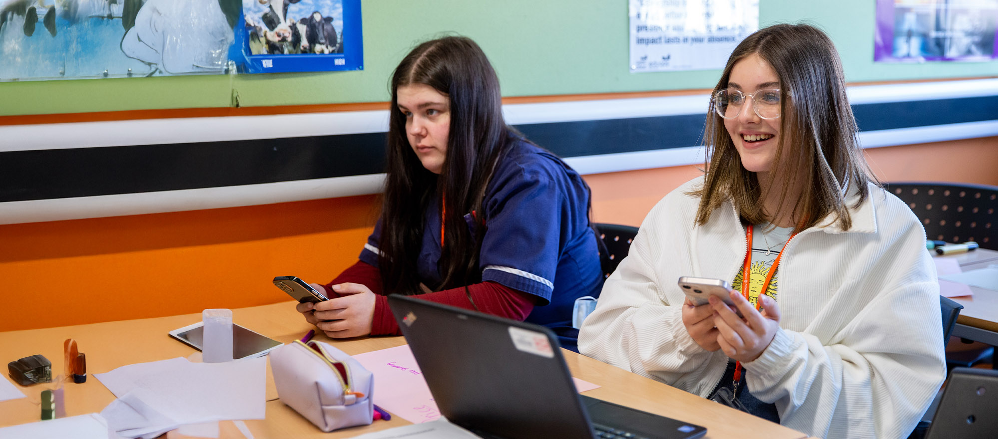 Student holding phone at computer in classroom