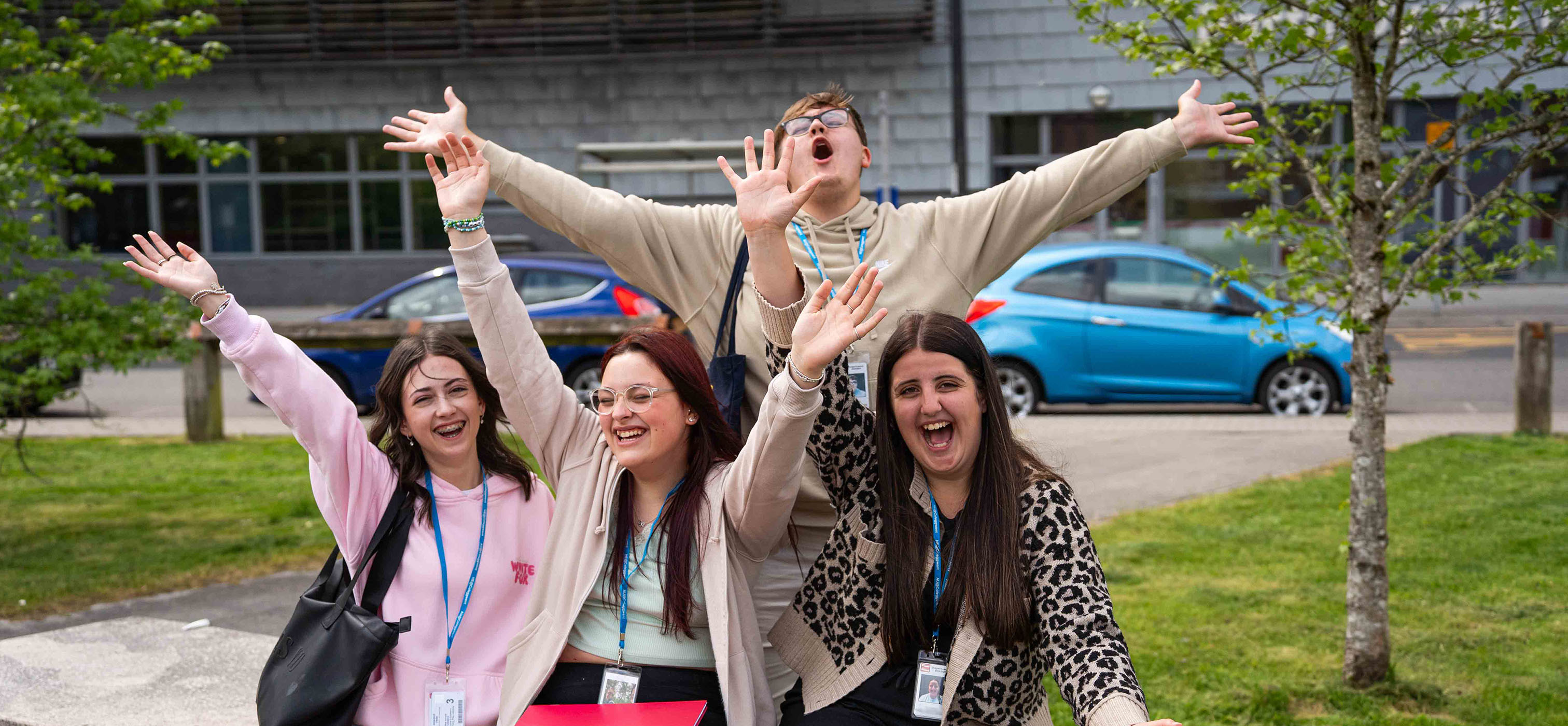 Students smiling outside BGLZ with arms in the air